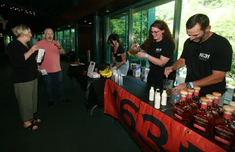 People gather around a table displaying bottles of bourbon, sampling and engaging with staff at an event.