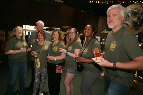 Group of people in matching green shirts socializing at an event, holding drinks and smiling.